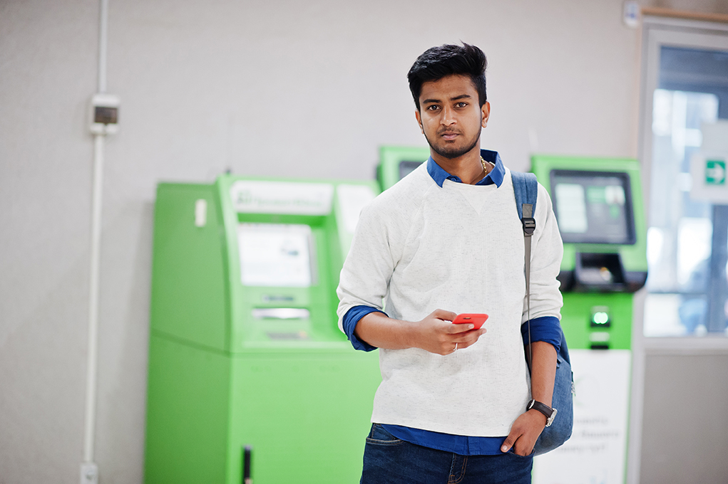 Young stylish asian man with mobile phone and backpack against r